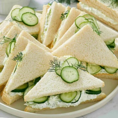 Plate of fresh cucumber sandwiches served with tuna and tomato slices.