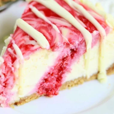 White Chocolate Raspberry Swirl Cheesecake topped with raspberry sauce and white chocolate