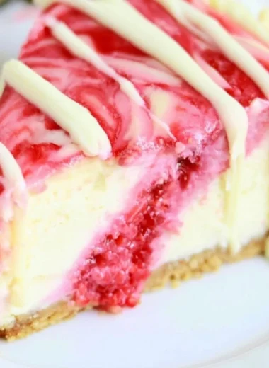 White Chocolate Raspberry Swirl Cheesecake topped with raspberry sauce and white chocolate