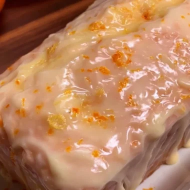 Freshly baked orange loaf cake topped with orange zest and icing.